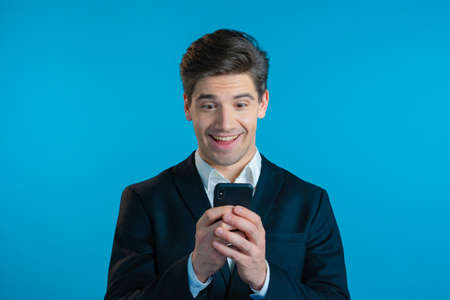 Handsome business man receives happy notification on mobile phone. Guy is beside himself with...