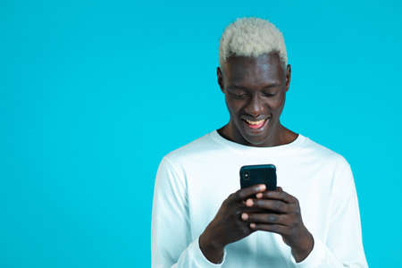 Handsome african man playing game on smartphone on blue studio wall. Using modern technology - apps,...