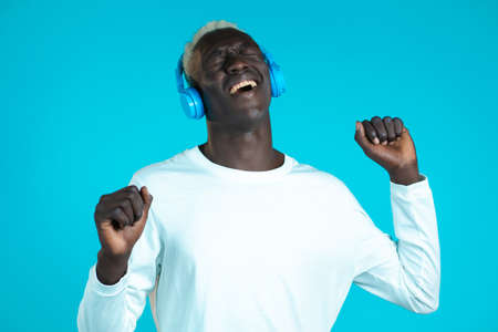 Handsome black man with trendy hairdo having fun, smiling, dancing with headphones in studio against...