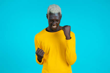 African american man in yellow is very glad and happy, he shows yes gesture of victory, guy achieved...