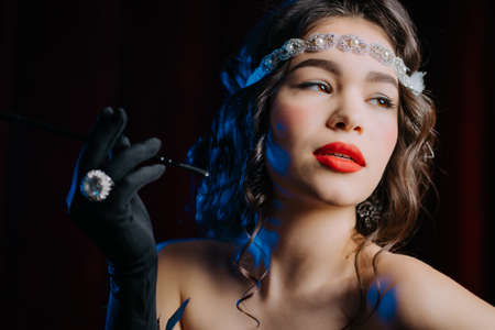 Brunette woman with mouthpiece cigarette dressed in style of twenties years flirting and posing on velours background. Roaring twenties, retro, party, fashion conceptの写真素材