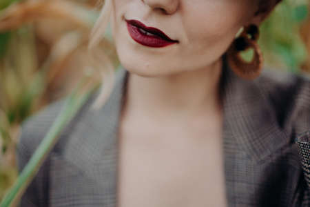 Dark red lips of trendy unrecognizable woman in jacket at natural corn background