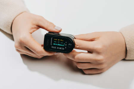 Woman put on pulse oximeter on finger, check blood oxygen saturation. Monitoring heart rate at home during pandemic coronavirus covid-19の写真素材