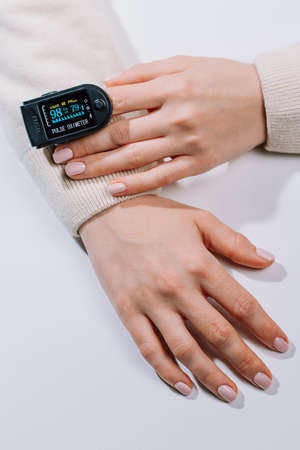 Woman put on pulse oximeter on finger, check blood oxygen saturation. Monitoring heart rate at home during pandemic coronavirus covid-19の写真素材