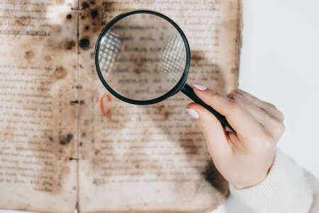 Woman researcher explores antique book with magnifier. Scientific translation of literature. Investigating manuscript with ancient writingsの写真素材