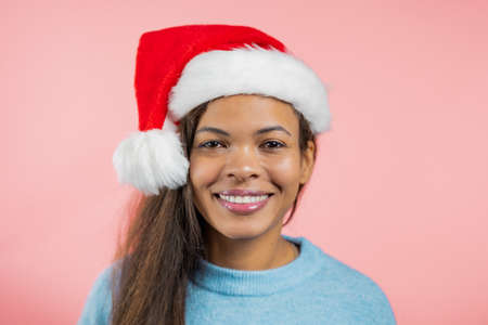 African woman in Santa hat looking to camera, smiling. Beautiful mature model lady on pink studio background. new year, Christmas concept,の写真素材