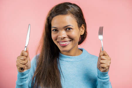 Portrait of hungry woman with fork and knife. Mature lady waiting for serving dinner dishes with...