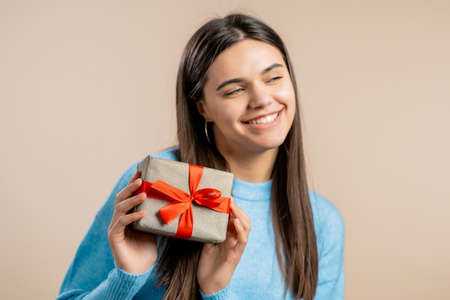 Excited woman received gift box with bow. She is happy and flattered by attention. Girl smiling with...