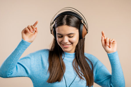 Cute woman dancing with headphones on light studio background. Cute girls portrait. Music, radio, happiness, freedom, youth concept.の写真素材