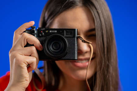 Young pretty woman takes pictures with DSLR camera over blue background in studio. Girl smiling as...