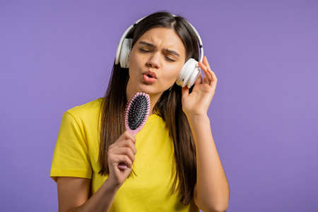 European woman singing and dancing with hair brush or comb instead microphone at violet studio...