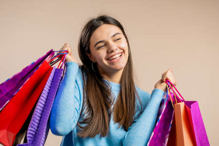 Happy woman with colorful paper bags after shopping on beige studio background. Concept of seasonal sale, purchases, spending money on giftsの写真素材