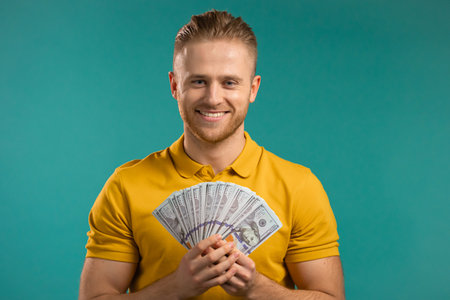 Happy excited man with cash money - USD currency dollars banknotes on blue wall. Symbol of jackpot, gain, victory, winning the lotteryの写真素材