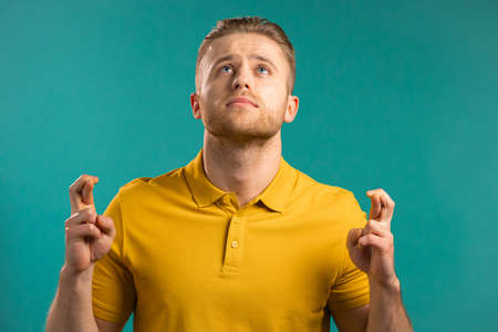 Young man praying over blue background. Guy begging someone satisfy his desires, help with.の写真素材