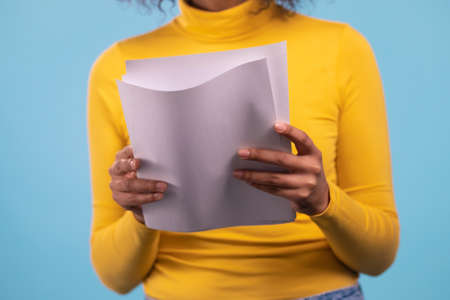 African woman holding files papers isolated on blue background. Girl checks documents, utility bills.の写真素材