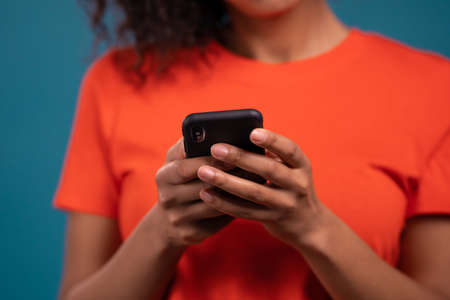 Hands of african woman using mobile phone on blue background. Technology, success, victory,...