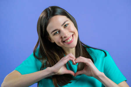 Kind pretty woman making sign of shape heart near her chest. Violet background. Women health,...