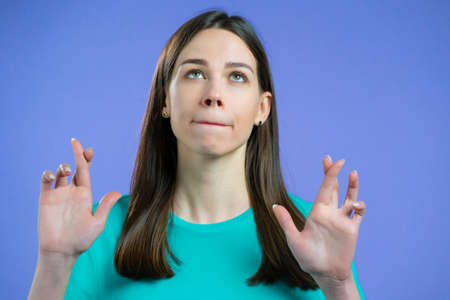Cute woman praying with crossed fingers over violet background. Girl begging someone satisfy her...