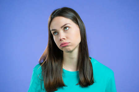 Portrait of girl, she exhales from heat or stuffiness. Heatstroke concept. Violet studio. Young tired woman is dissatisfied, unhappy.の写真素材