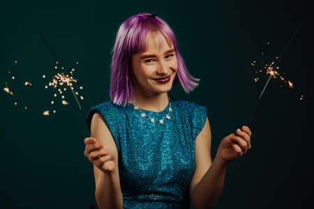Hipster woman with sparkling bengal fire on green background. Christmas holiday concept. Young dyed...