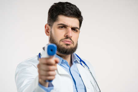Doctor man in white medical coat directs electronic non-contact thermometer into camera lens and...