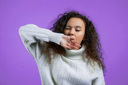Tired sleepy woman yawns, covers her mouth with hand. Very boring, uninteresting. Violet studio background.の写真素材