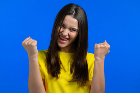 Woman is very glad and happy, she shows yes gesture of victory, she achieved result, goals. Surprised excited happy lady on blue studio background. Jackpot concept.の写真素材