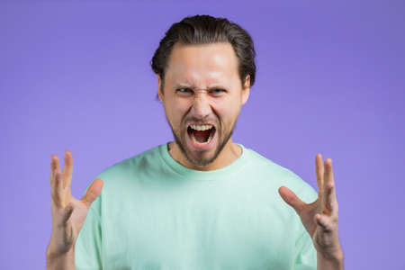 Man in rage on violet background. European guy in stress, he is in aggression and looking at camera...