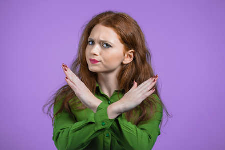 Pretty girl disapproving with no crossing hands sign make basta, negation, enough gesture. Denying, Rejecting, Disagree, Portrait of pretty woman on violet backgroundの写真素材