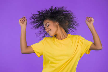 Happy curly haired african woman dancing, having fun, rejoices on purple studio background. Champion...