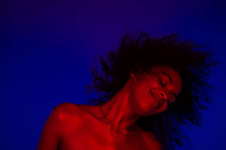 Cool disco dancing unique afro woman under neon glowing light. Multi colored shot of lady moving to...