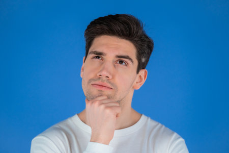 Thinking man looking up on blue background. Pensive face expressions. Handsome guy in white wear.の写真素材