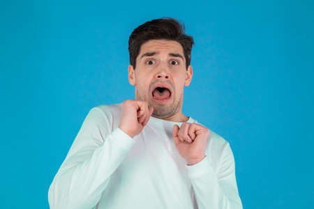 Frightened european man afraid of something and looks into camera with big eyes full of horror over blue wall background.の写真素材