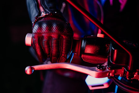 Motorcyclist hand wearing leather gloves twists accelerometer lever in colored city lights. Camera moving along handlebars of motorcycle. Nightlife and biker culture concept.の写真素材