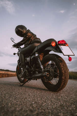 Stylish motorcyclist woman in helmet and leather jacket sitting on vintage motorcycle. Female driver...