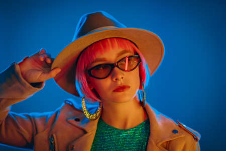 Portrait of glamorous woman on party under glowing neon light. Nightclub, trendy outfit. Teenager, zoomer Z-generation. Lady in hat and glasses.の写真素材