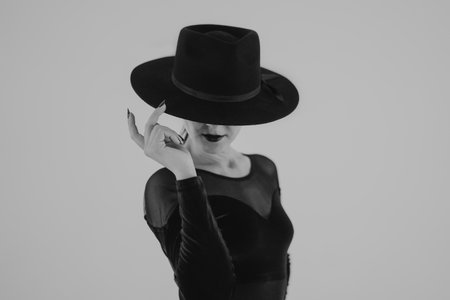 Charming woman posing with black hat on white background. Femme fatale costume, stylish outfit. Black and white. Sexy model dancer.の写真素材