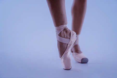 Ballet dancer's feet in pointe shoes close-up, she posing on tiptoes isolated on blue studio background. Beautiful woman's legs. Unrecognizable ballerina. High quality photoの写真素材