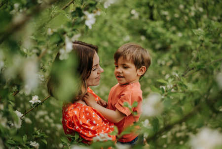 Beautiful touching scene of mom and toddler son in blooming spring garden. Happy mother and baby boy embracing. Family, love, childhood concept.の写真素材