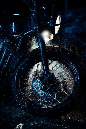 Vintage styled motorcycle on washing. Blue illumination at night. Splashing water on front wheel with disc brakes. Classic black motorbike. Caferacers style. Maintenance of motor vehiclesの写真素材