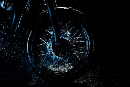 Motorcycle at wash after off-road driving. Cold blue lighting. Washing front wheel with disc brakes with water. Classic black motorbike. Caferacers style. Maintenance of motor vehicles. Copy space.の写真素材