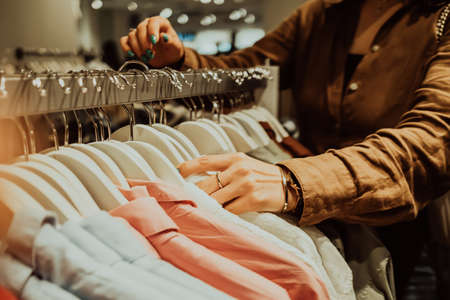 Young woman in fashion store chooses things for herself - white cotton shirt. Customers, shopping, sales concept.の写真素材