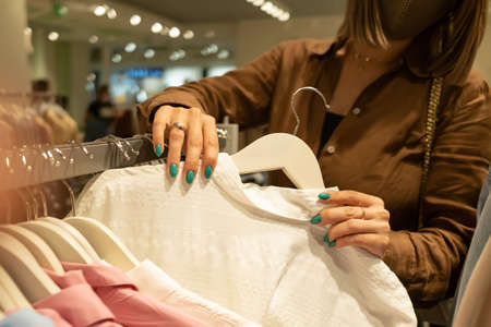 Young woman in fashion store chooses things for herself - white cotton shirt. Customers, shopping, sales concept.の写真素材