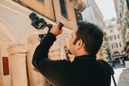 Male cameraman shoots urban architecture and building facades with steadicam on mirrorless camera. Greece or Italy background.の写真素材