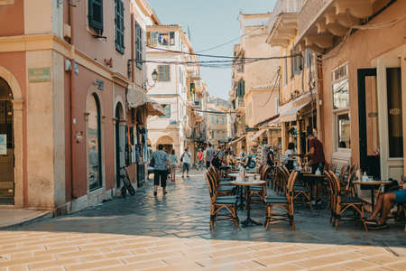 Corfu, Greece - September 2021. Beautiful cozy narrow street in old greek town. Historic european centre with cafe and people, tourists. Cityscape concept.のeditorial素材