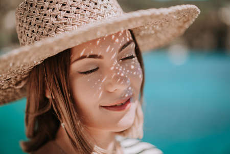 Pretty woman in straw hat smiling sincerely on blue sea background. Girl enjoying fresh air, breeze. Lady on luxury travel destination, vacation lifestyle concept.の写真素材