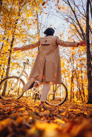Young pretty woman enjoying autumn nature near vintage white bicycle. Lady having fun on orange nature fall background in park.の写真素材