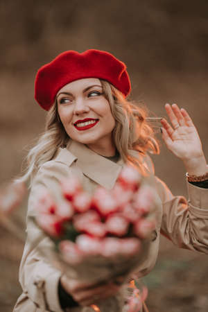 Young pretty woman in red beret, beige classic trench coat and bouquet of tulips. Girl on date. International Womens Day. Retro Parisian Style.の写真素材