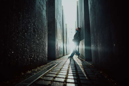 October 2021 - Berlin, Germany. Woman stands in dark maze between tall blocks in Holocaust Jewish Memorial of Murdered Jews. Light at the end of tunnel.のeditorial素材