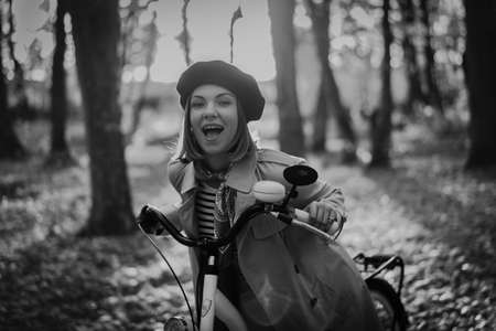 Beautiful black and white portrait of young smiling woman in french beret cycling alone in park. Sunny day in forest. Trendy lady on vintage bicycle, healthy lifestyle, aesthetic sceneの写真素材